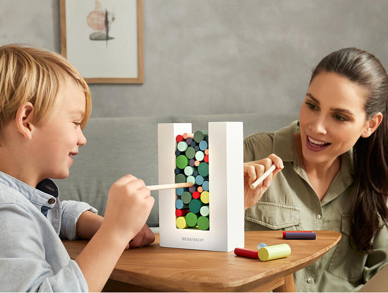 Een kind en een volwassene spelen samen met het Woodman vaardigheidsspel aan een tafel.