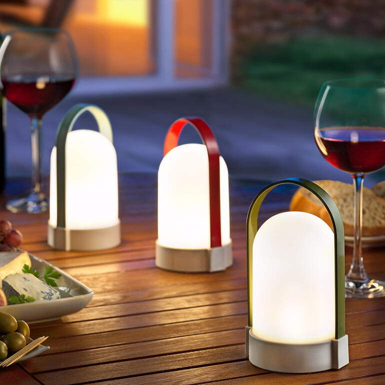 Drie Piccolos acculampen op een tafel buiten, omringd door voedsel.