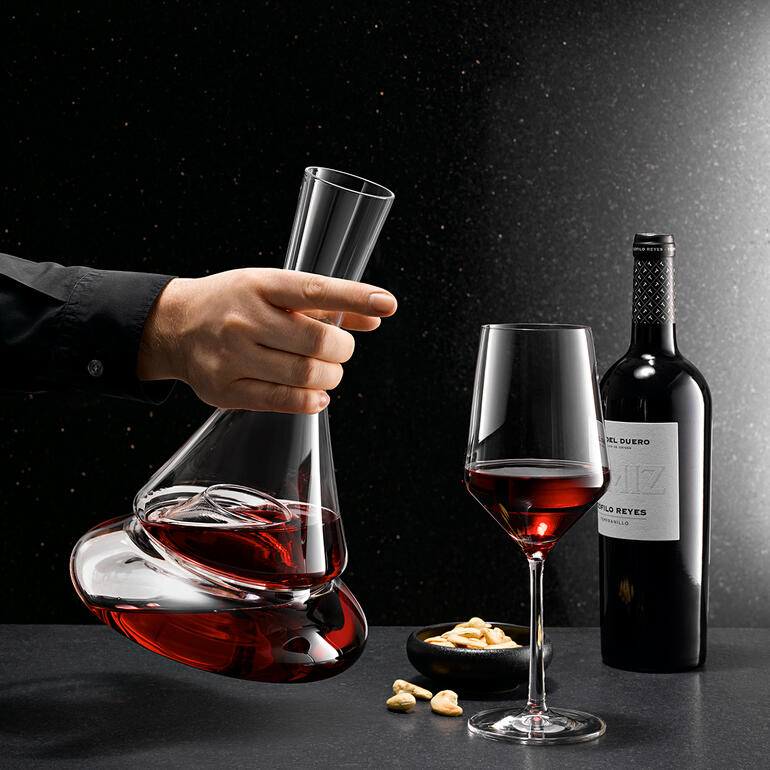 Doppio dubbele decanter met rode wijn in de hand, naast een wijnglas en noten.