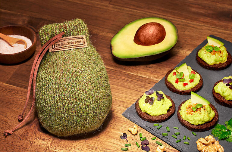 Avocado Sock® samen met avocado en snacks op een houten tafel.