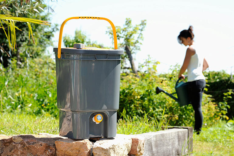 BioMix vloeibare meststofbereider in een tuin, vrouw werkt op de achtergrond.