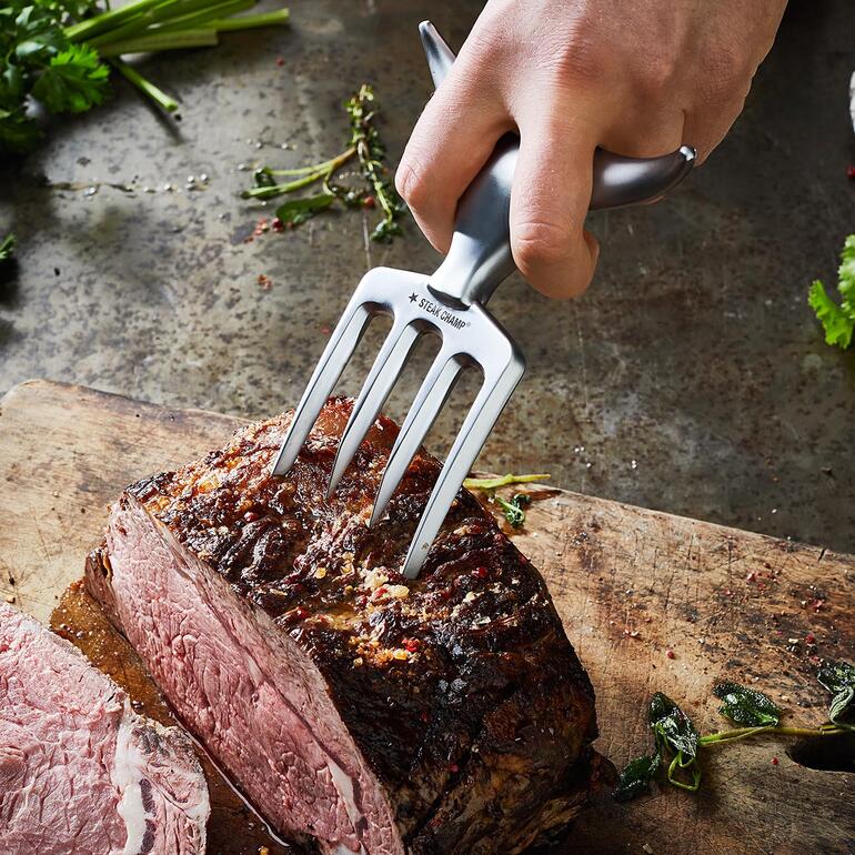 Met de sterke tanden steekt u moeiteloos in grote stukken vlees. Hand houdt Bull Fork vast om een stuk vlees te snijden.