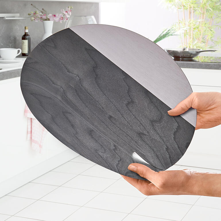 Trendy 2-kleurige uitvoering. Hand houdt het ovale tafelset van hout met zilveren en zwarte afwerking.