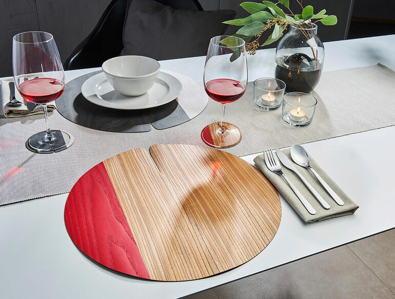 Tafelset van hout met rode en lichte houtkleur op een gedekte tafel met glazen en servies.