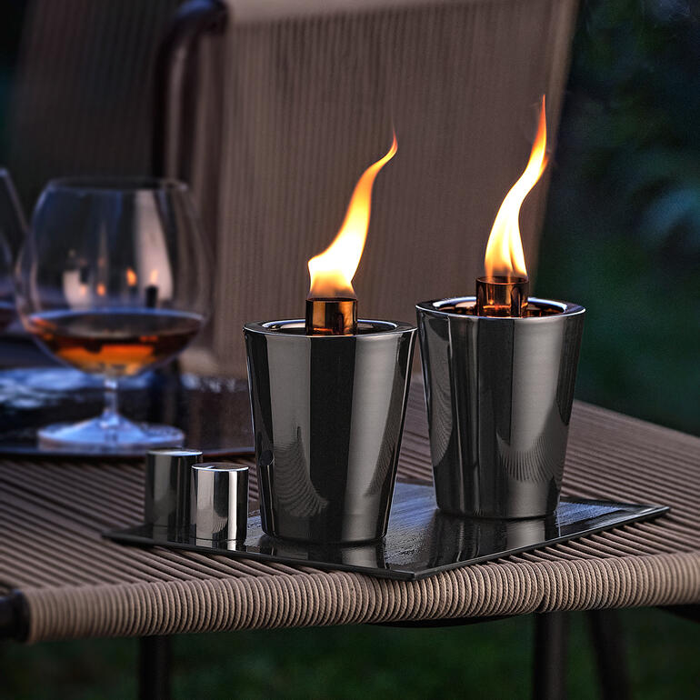 Tafel fakkels op een tafel in een buitenruimte met een cocktailglas op de achtergrond.