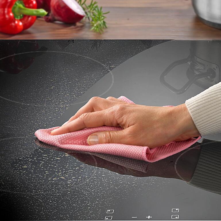 Hand veegt met een vetweg-doek over een kookplaat.