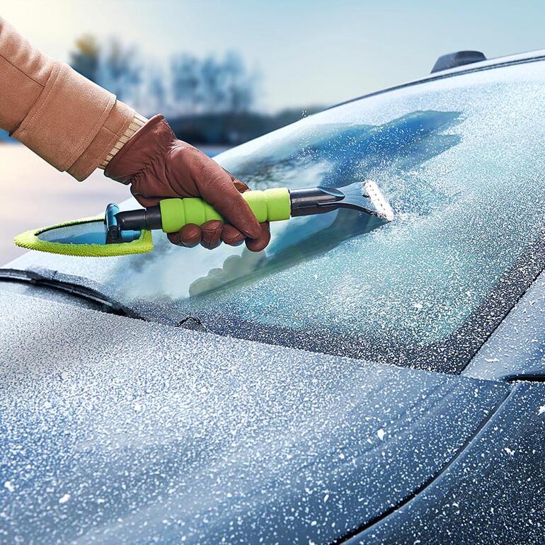 Hand met een gecombineerde ruitenwissers die vorst van de autoruit verwijdert