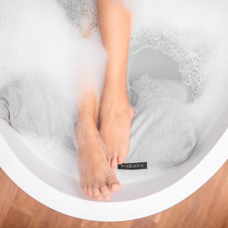 Close-up van voeten in schuim en badsofa-kussen in bad.