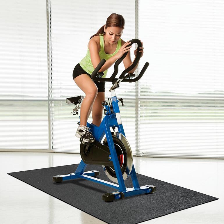 Vrouw op een spinningfiets op een recycle-bodembeschermmat.