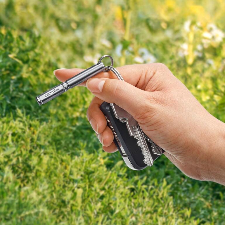 Hand houdt ZECKstick en een zwarte sleutelhanger buiten vast.