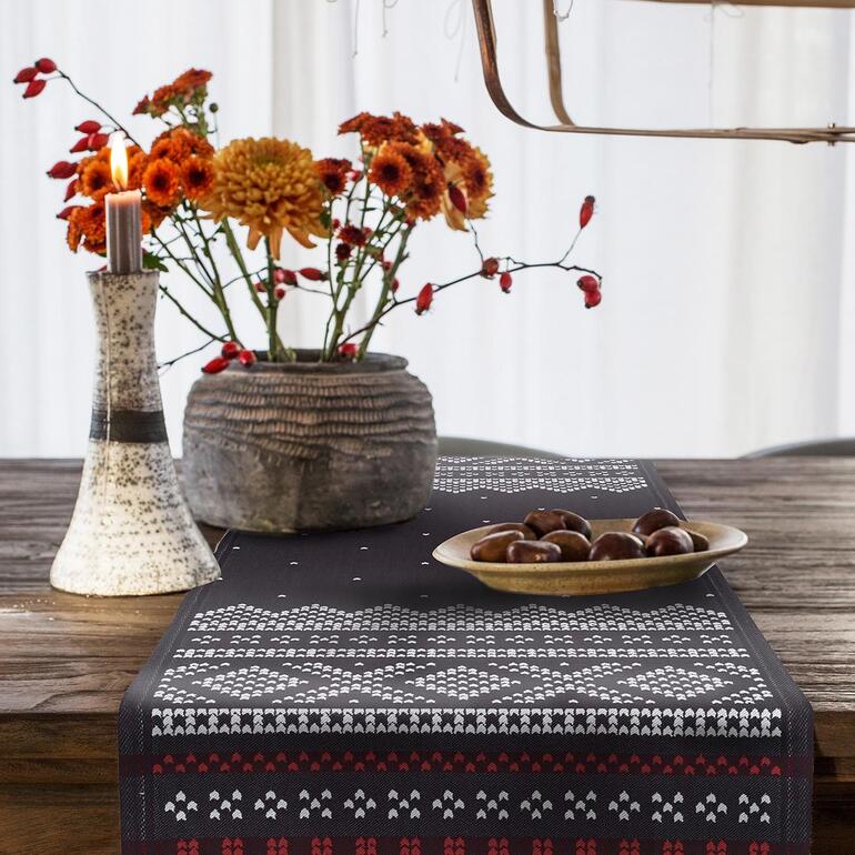Met zorgvuldig afgezette randen en zwaar geweven materiaal, zodat de loper altijd onberispelijk glad ligt. Tafel met zwart Noorwegen tafelkleed, kaars en boeket bloemen.