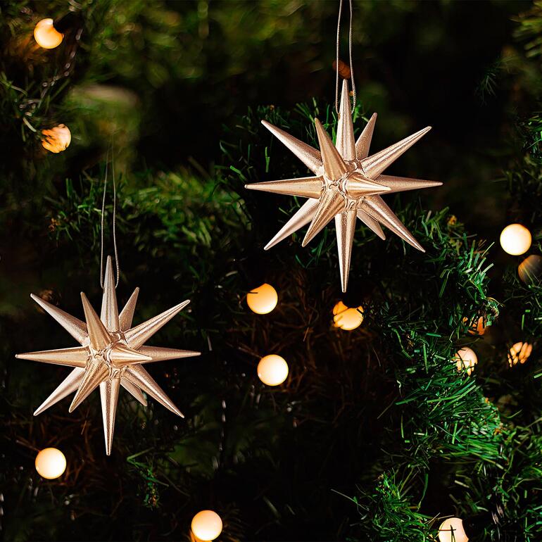 Twee gouden Seiffener kerststerren hangen aan een dennenboom.