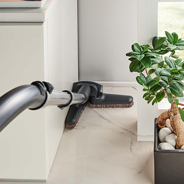 In hoeken en nissen klapt de Flex-zuigmond in en uit, zodat u niet hoeft te bukken en meubels niet hoeft te verplaatsen. Flexibele stofzuigermond die in de hoek van een kamer wordt gebruikt.