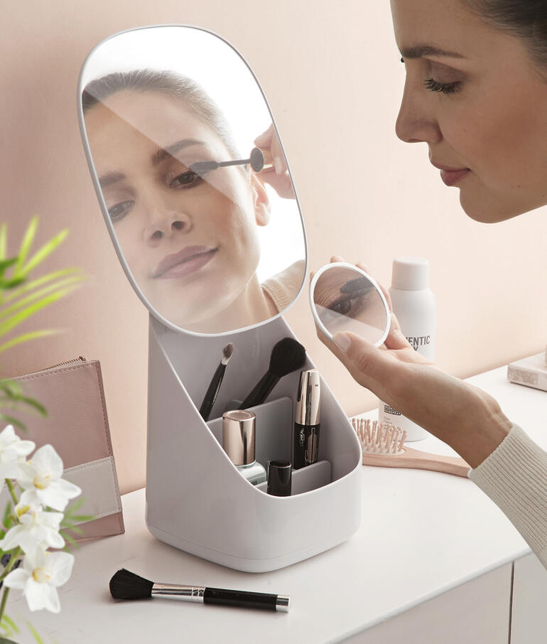 Vrouw maakt zichzelf op voor een make-up spiegel met geïntegreerde organizer op een tafel.