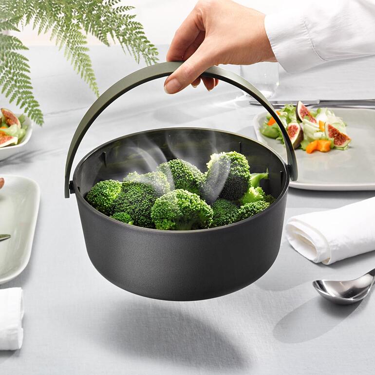Het handvat wordt niet heet, dus de stoompan is gemakkelijk te vervoeren. Magnetron stoomkoker met handvat die broccoli serveert