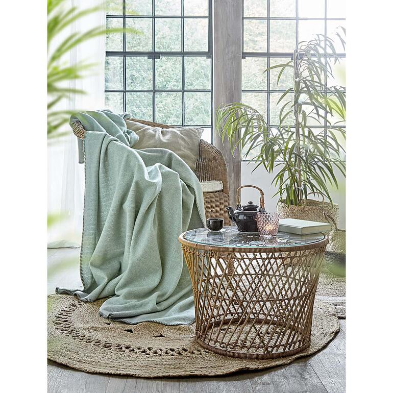 salie Wollen fleece deken op een fauteuil naast een exotische plant.
