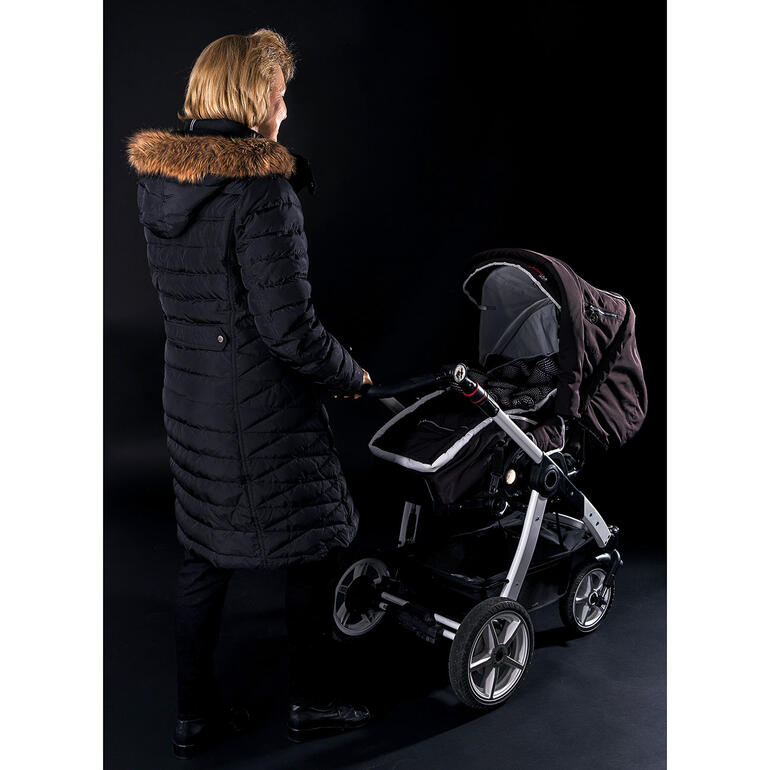 Zonder kinderwagen–veiligheidsvest. Vrouw met kinderwagen zonder waarschuwingsvest, op een donkere achtergrond.