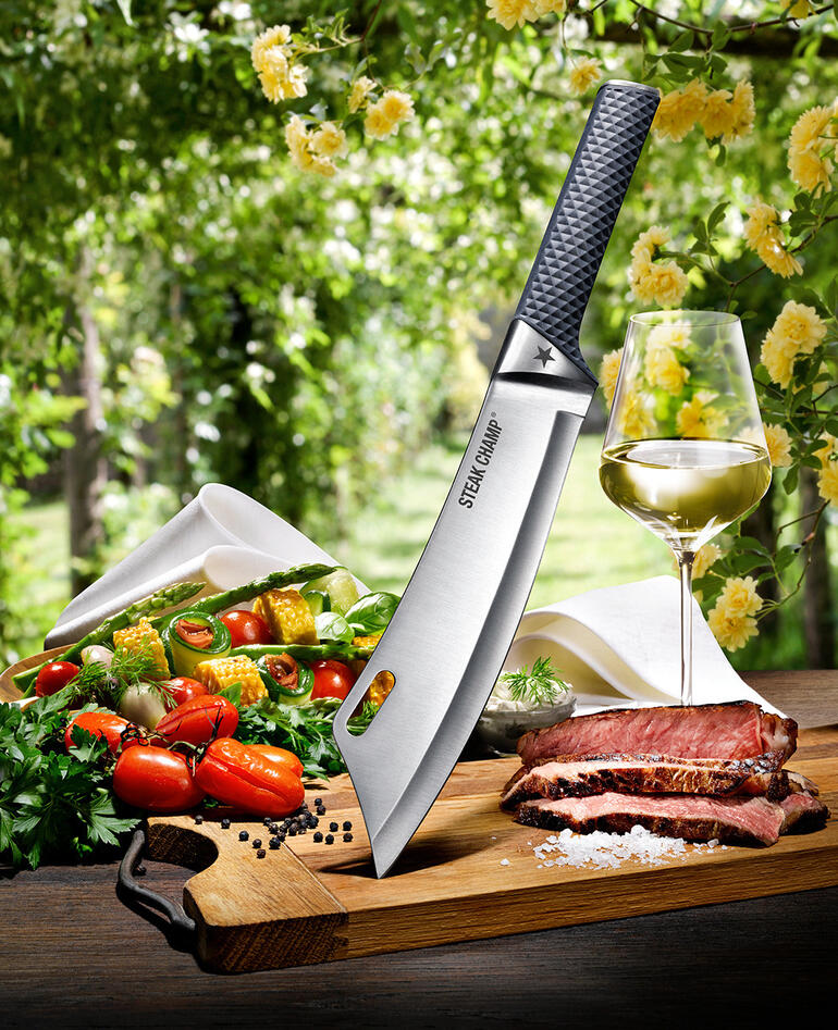 SteakChamp koksmes van bovenaf, omringd door groenten en vlees op een snijplank.