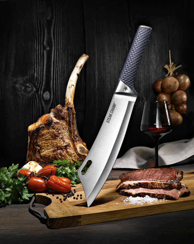 SteakChamp koksmes BBQ Pro SteakChamp koksmes op een snijplank, naast een stuk vlees en een fles wijn.