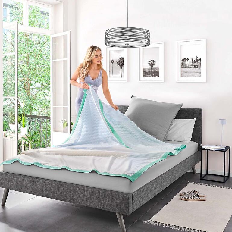 Vrouw vouwt de Breezyblanket op een bed.