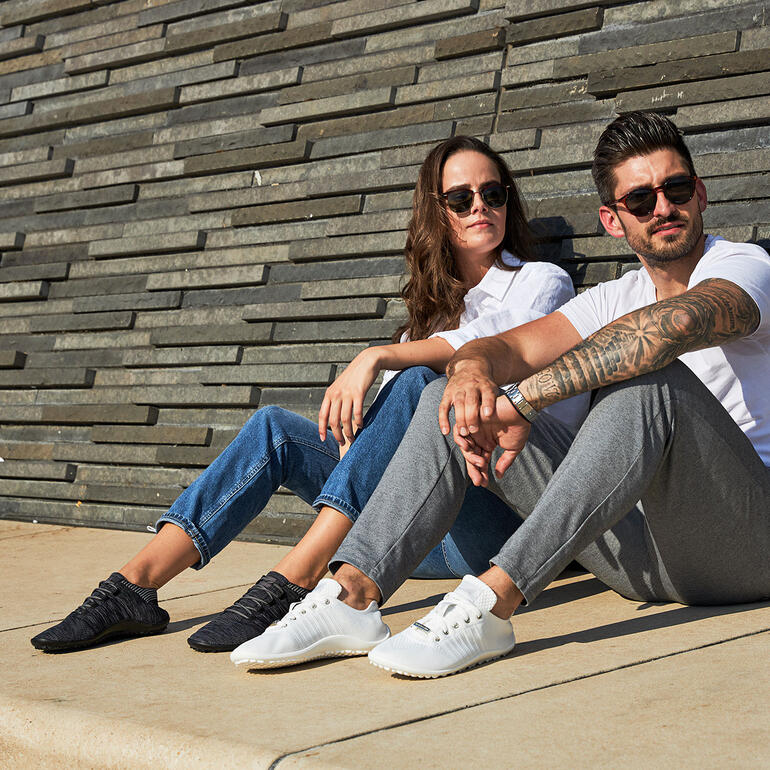 Twee personen met Barfuß-leguano Sneakers zittend aan een muur.