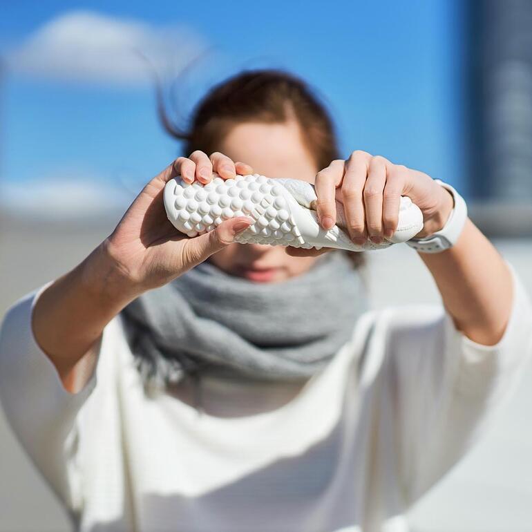 Een persoon houdt een Barfuß-leguano Sneaker in wit met beide handen vast.