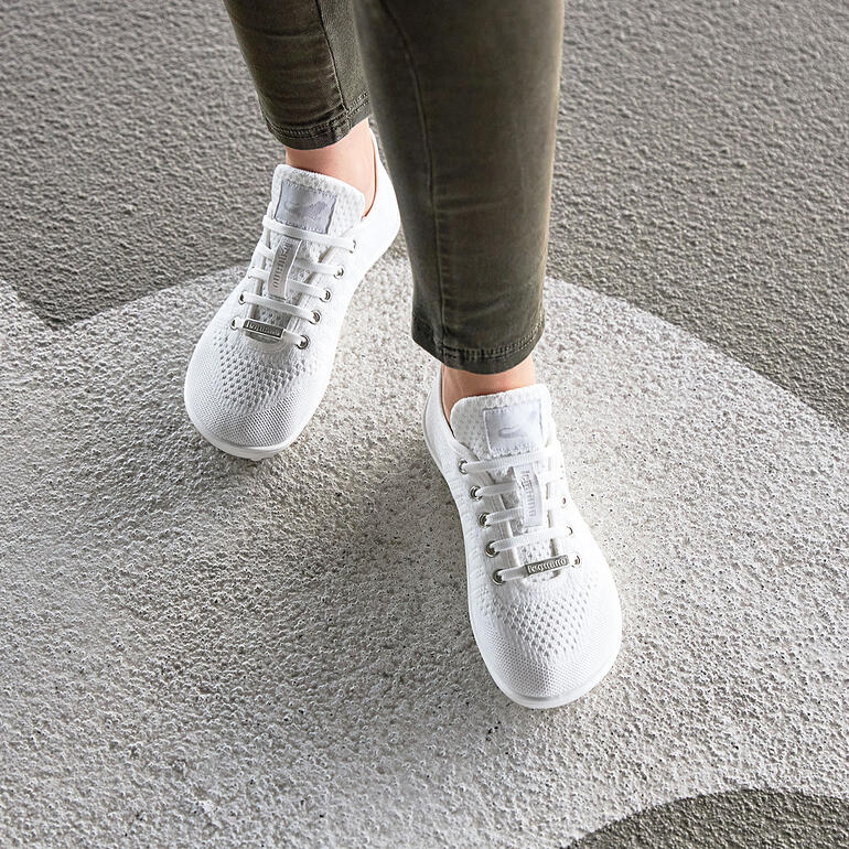 Persoon draagt witte Barfuß-leguano® sneakers op een grijze vloer.