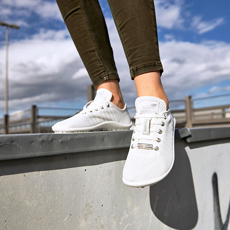 Persoon staat op een reling en draagt witte Barfuß-leguano® sneakers.
