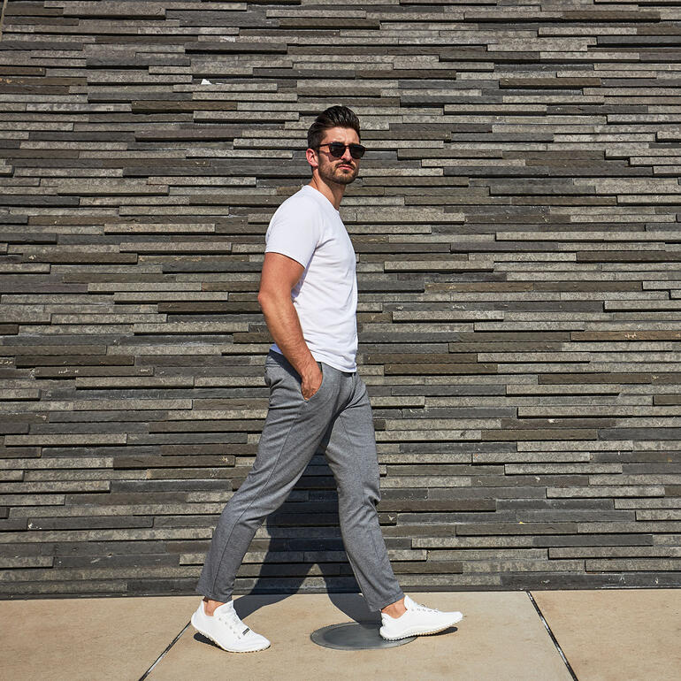 Man loopt voor een stenen muur met witte Barfuß-leguano® sneakers.