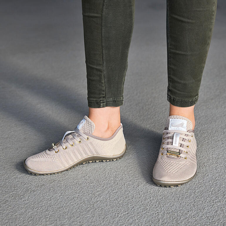Persoon draagt beige Barfuß-leguano® sneaker op een grijze vloer.