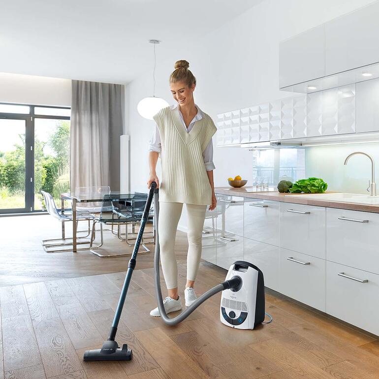 Vrouw gebruikt een vloerzuiger in een moderne keukenruimte.