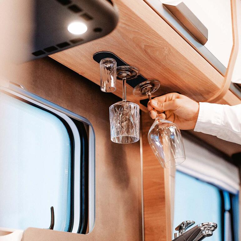 Hand neemt een hangend kristallen glas in een camper