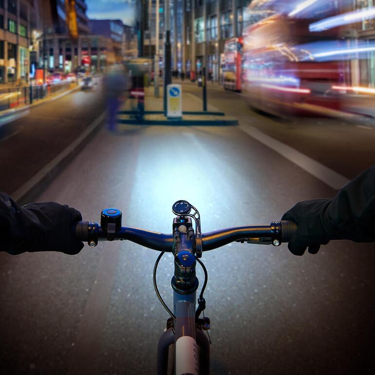 Kan centraal op het stuur worden geplaatst – voor extra optimalisatie van de verlichting. Gezicht vanaf het fietsstuur op een verlichte stadsweg in de schemering.