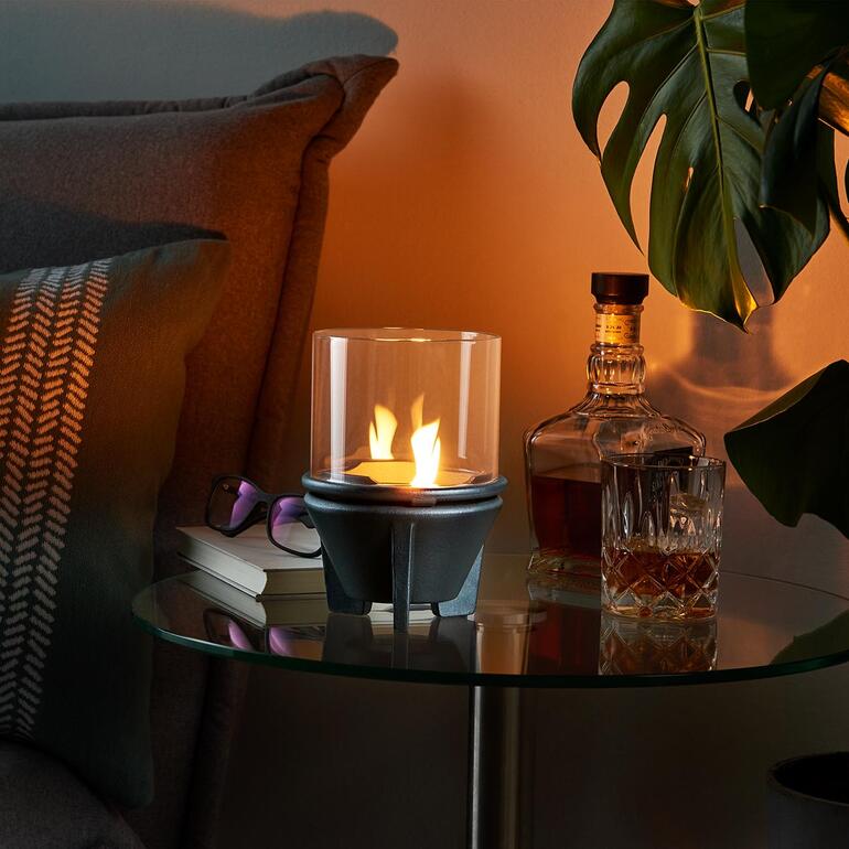 Smeltvuur met glazen cilinder op een tafel naast whiskey en planten.