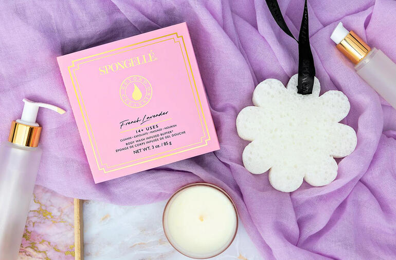 Spongellé schoonheidsspons in een roze verpakking, omringd door cosmetische producten.