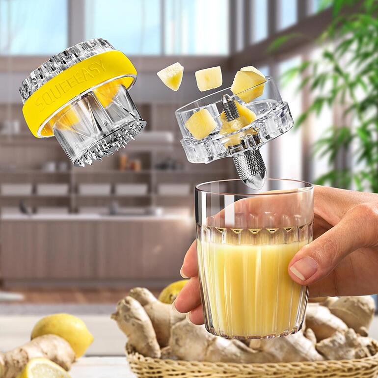 Hand die een glas met vers geperst gembersap vasthoudt, terwijl de gemberpers zweeft.