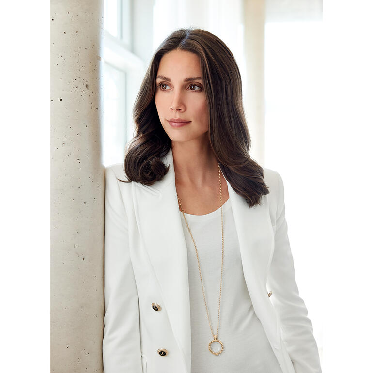 De elegante ketting met kristalheldere siersteen is tevens een vergrootglas voor 6-voudige vergroting. Vrouw in witte blazer draagt een vergrootglas ketting om haar nek.