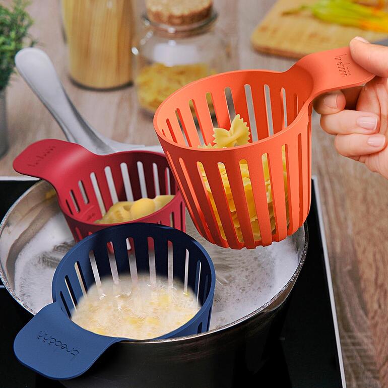 De verschillend gekleurde manden kunt u gewoon aan de rand van de pan hangen. Drie kookmanden in verschillende kleuren, één wordt boven een kookpan gehouden.