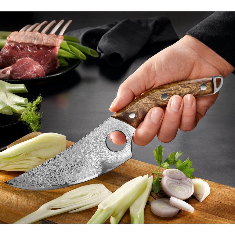 Damast slagersmes in de hand met verse ingrediënten op de achtergrond.
