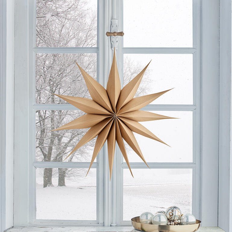Houten kerstster hangt voor een raam met winterzicht.