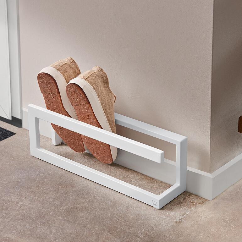 Schoenenrek met een paar beige sneakers die op een witte plank staan.