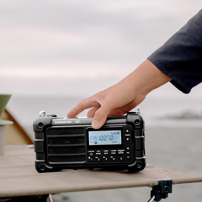 Hand die een digitaal survivalradio met LCD-display vasthoudt tijdens een outdoor-activiteit.