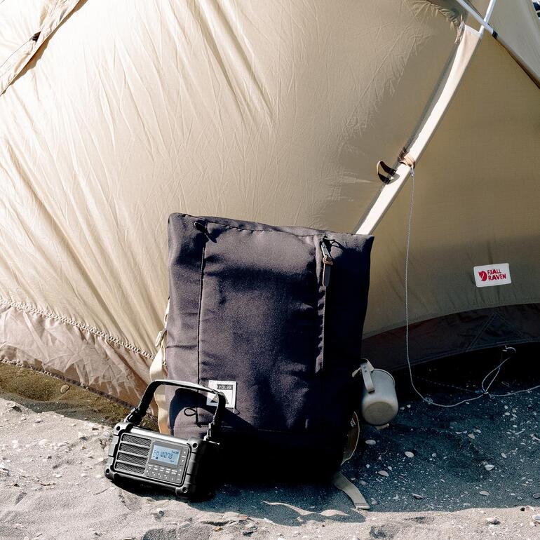 Digitale survivalradio naast een rugzak voor een tent buiten.
