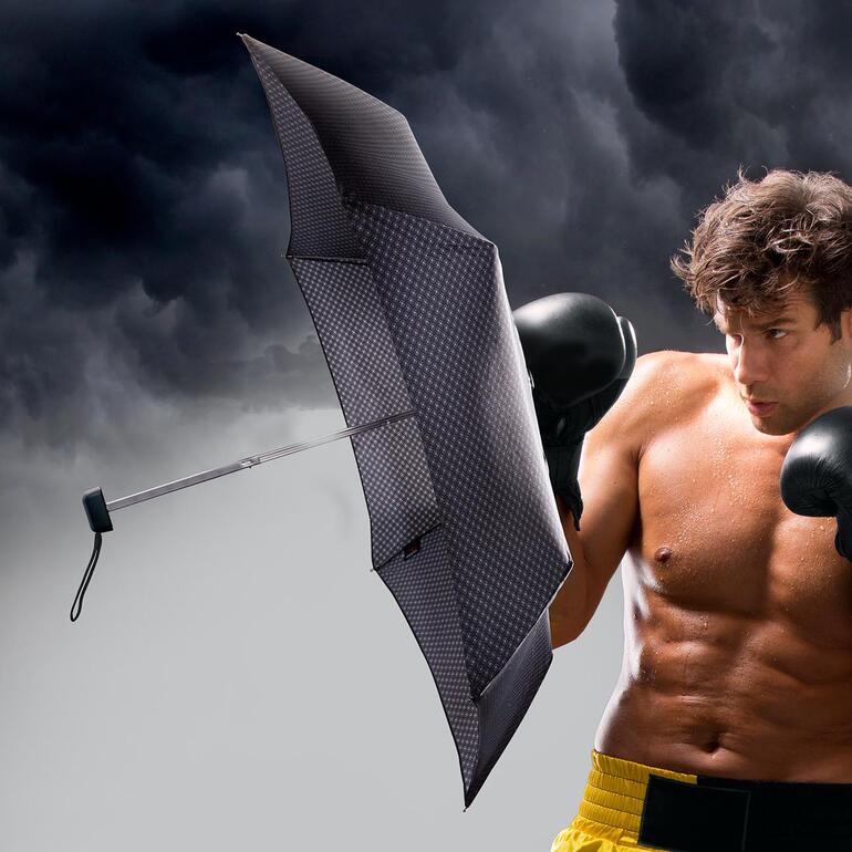 Man met carbonstalen tasparaplu in een stormachtige omgeving.