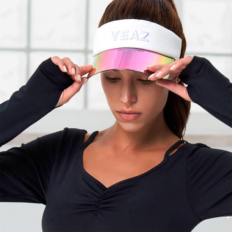 Vrouw met zonne-visor tilt deze een beetje op, in een zwart shirt.