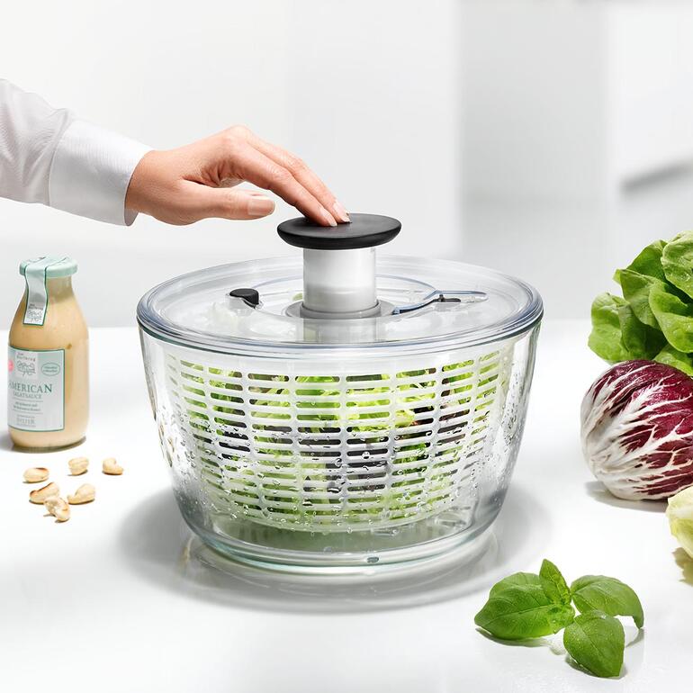 Vrouw draait de deksel van een glazen sla centrifuge met verse sla.