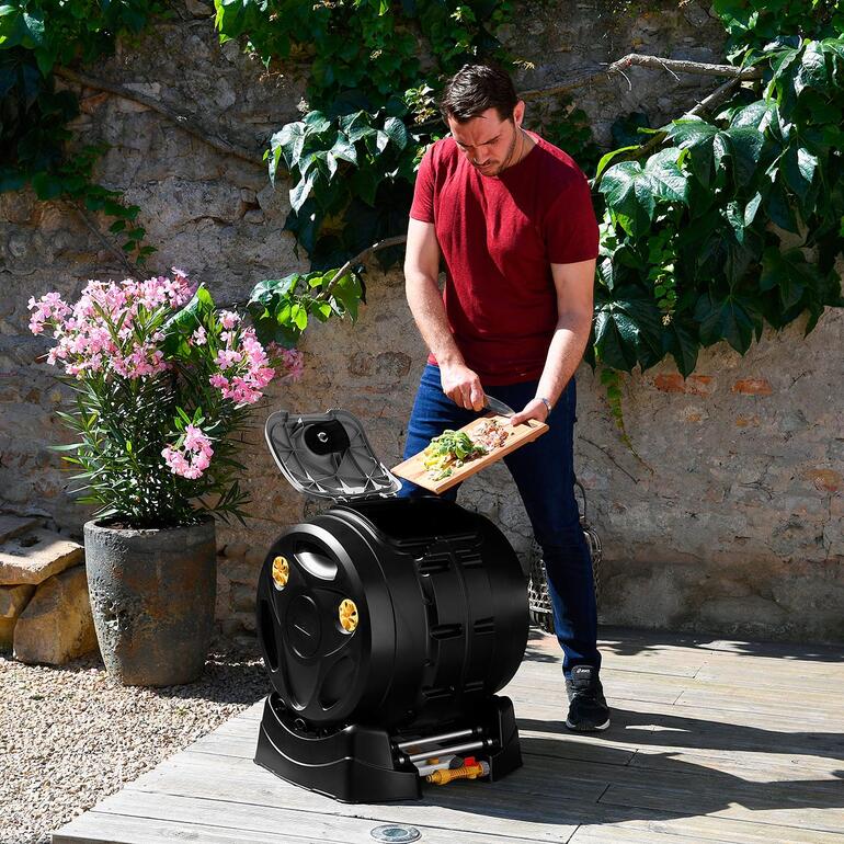 Man brengt keukenafval naar een 2-in-1 trommelcomposteerder in de tuin.