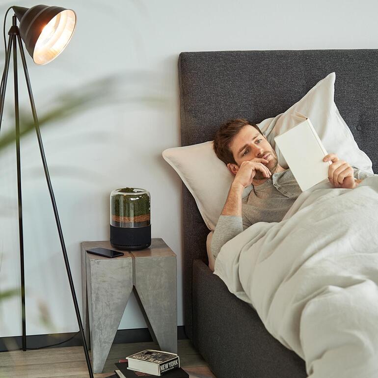 Man in bed leest een boek naast een natuurlijke luchtreiniger.