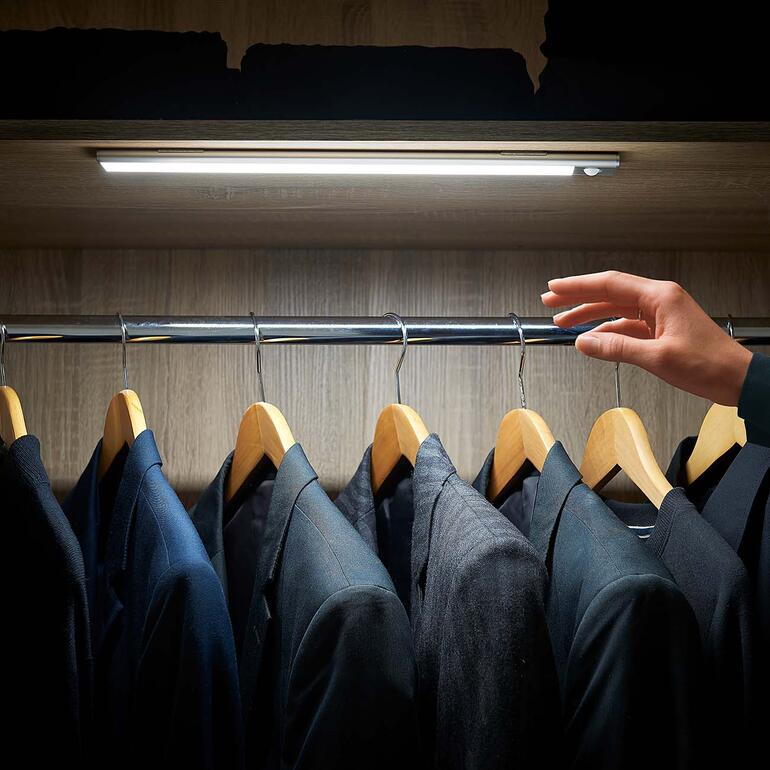 Variabele accu-verlichtingsbalk in de kast terwijl een hand een pak ophangt.