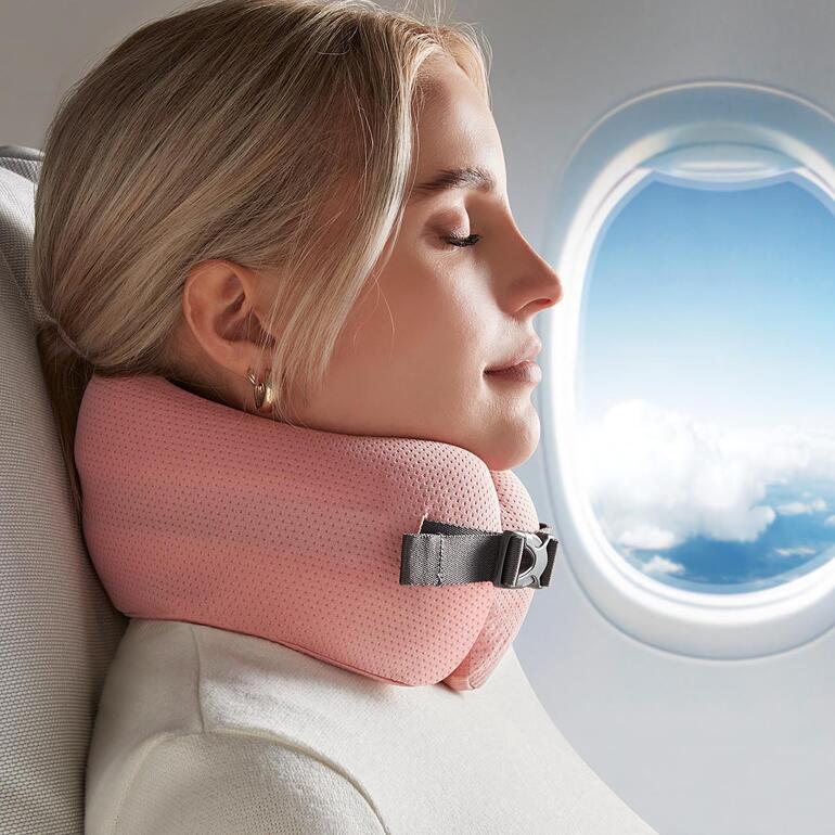 Vrouw met roze comfortabel reiskussen, ontspannen bij het raam in het vliegtuig.